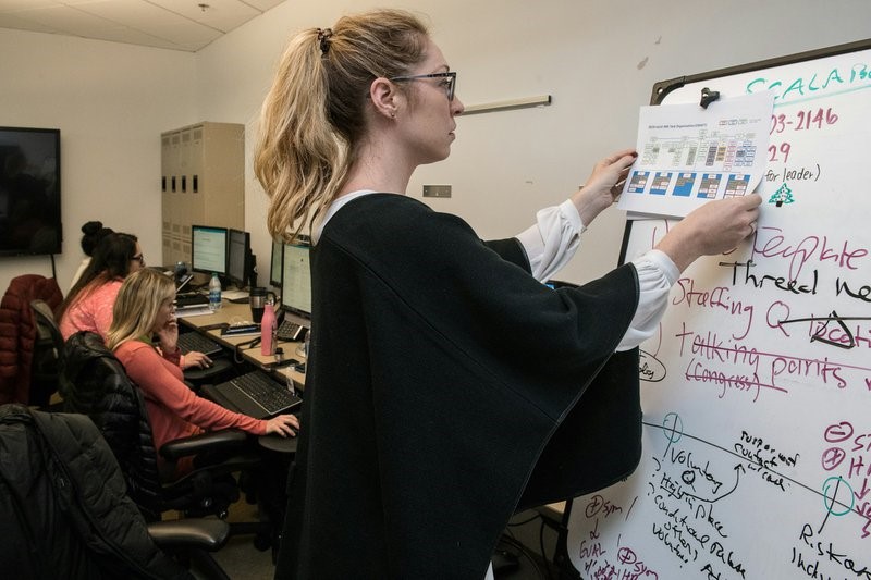 woman in black sweater writing on white board possibly planning for ISO compliance