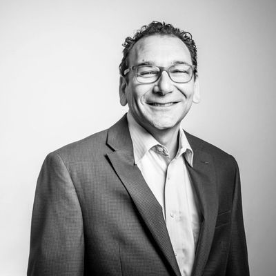 Black and white portrait of Norman Harber, a man wearing glasses, a suit jacket, and a collared shirt, smiling at the camera against a plain background.
