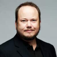 Matthew Ancelin, principal solutions architect at SecurityScorecard, with short, light brown hair and a trimmed beard, wearing a black jacket and black shirt, poses against a plain light gray background.