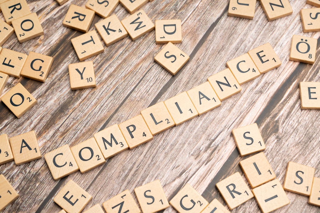 Scrabble tiles on a wooden surface spell the word COMPLIANCE in a straight line, surrounded by scattered tiles—capturing the essence of a compliance challenge.