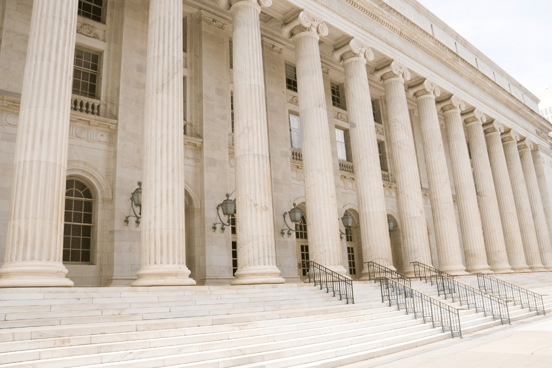 A grand neoclassical building with tall, white columns, ornate lanterns, and wide marble steps leading to large doors—its official presence evokes the security of a FedRAMP Certified institution.